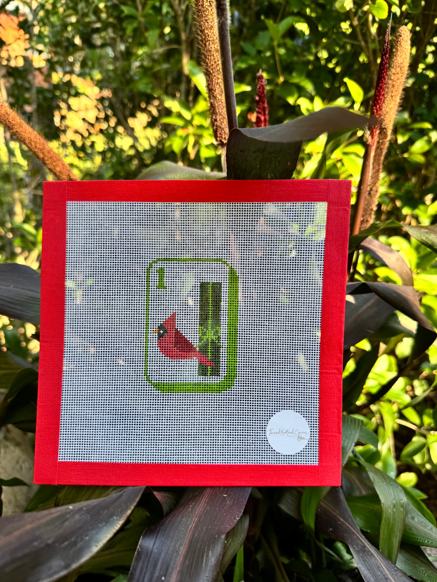 A square hand painted needlepoint canvas featuring a Mahjong Bird Bam red cardinal on a green tree branch, bordered by a red frame, 