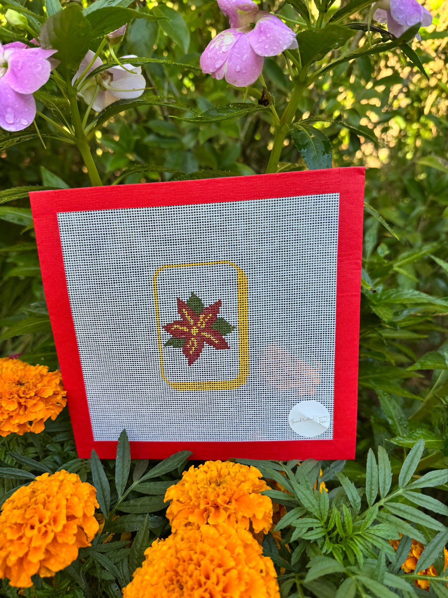 A hand painted needlepoint canvas with a red border and a Mahjong Flower Tile 